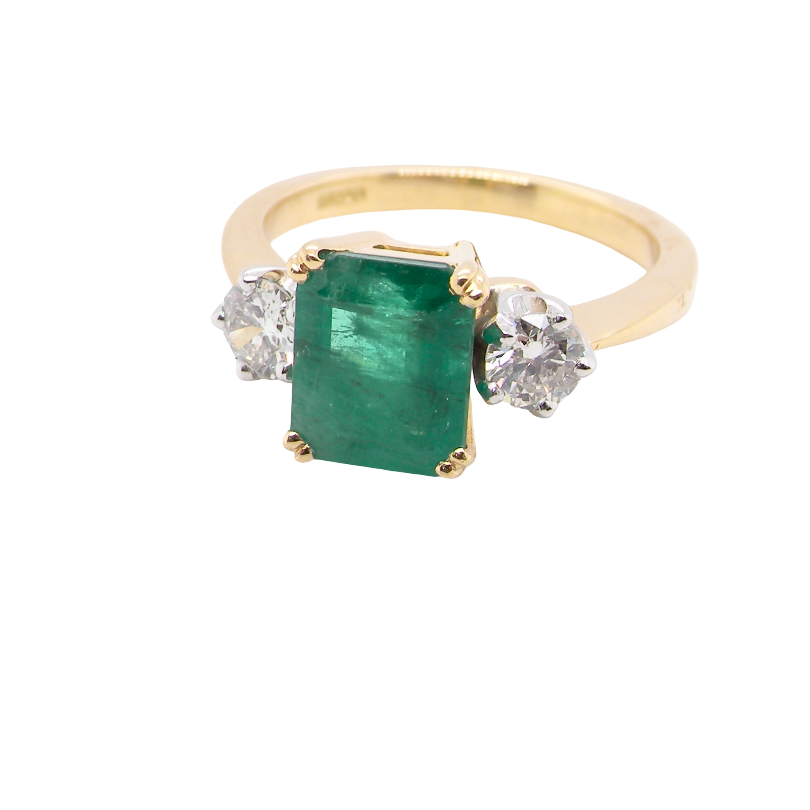 An exceptional three-stone ring featuring a vibrant step-cut emerald to the centre, measuring 8.6 x 7.0mm and weighing approximately 2.10 carats. The emerald displays a beautiful grass-green colour and is secured in a four-claw setting.