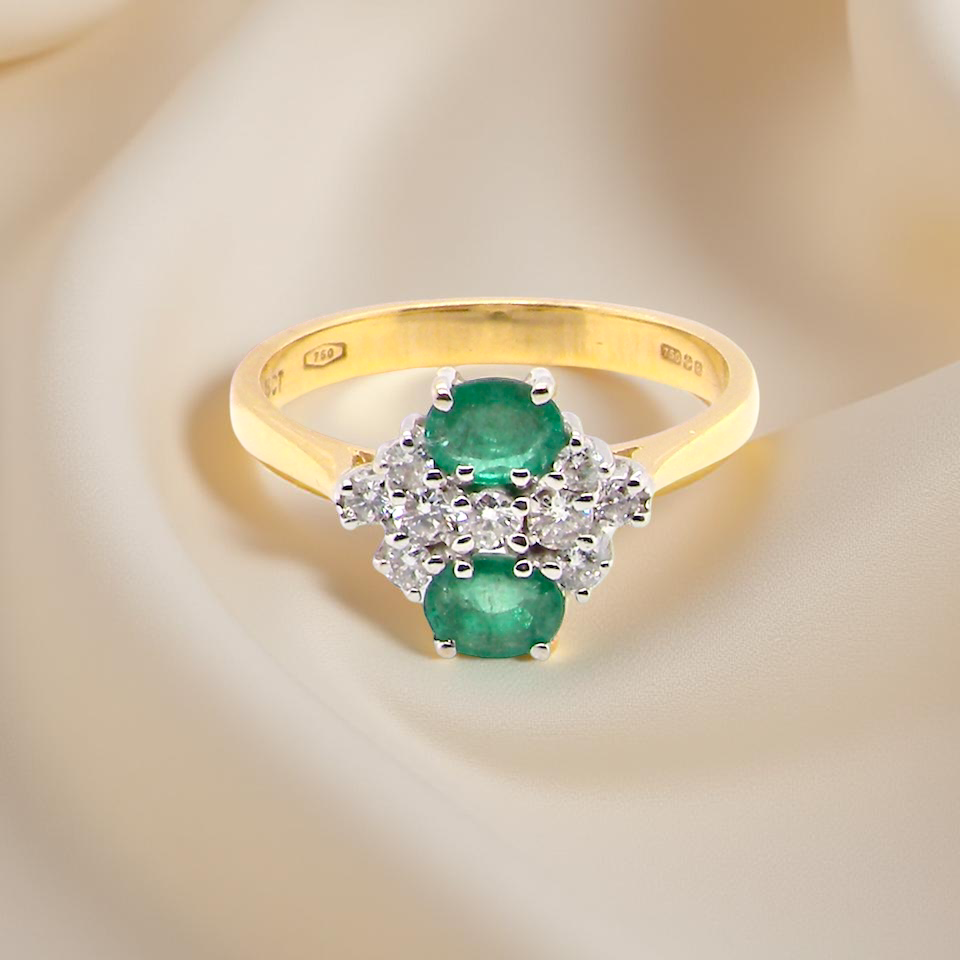 Gold ring with emeralds and diamonds on a soft beige background
