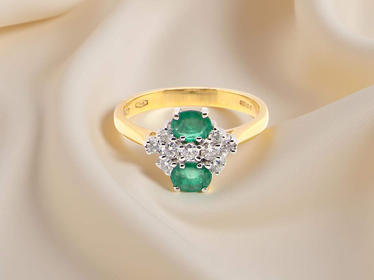 Gold ring with emeralds and diamonds on a soft beige background