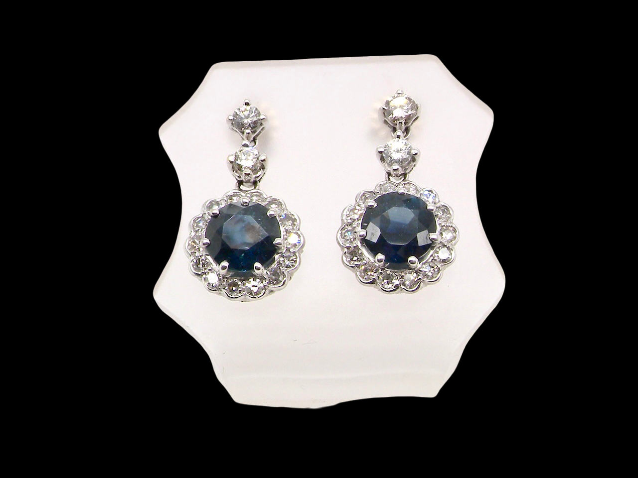 An exquisite pair of drop earrings crafted in 18 carat white gold, each set with a striking inky blue-black sapphire