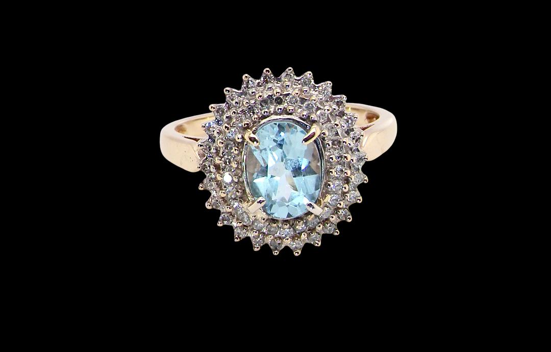 An impressive cluster ring that features to the centre an oval cut blue topaz gemstone, 8x6mm sky blue colour.
Complimented by a double halo of diamonds