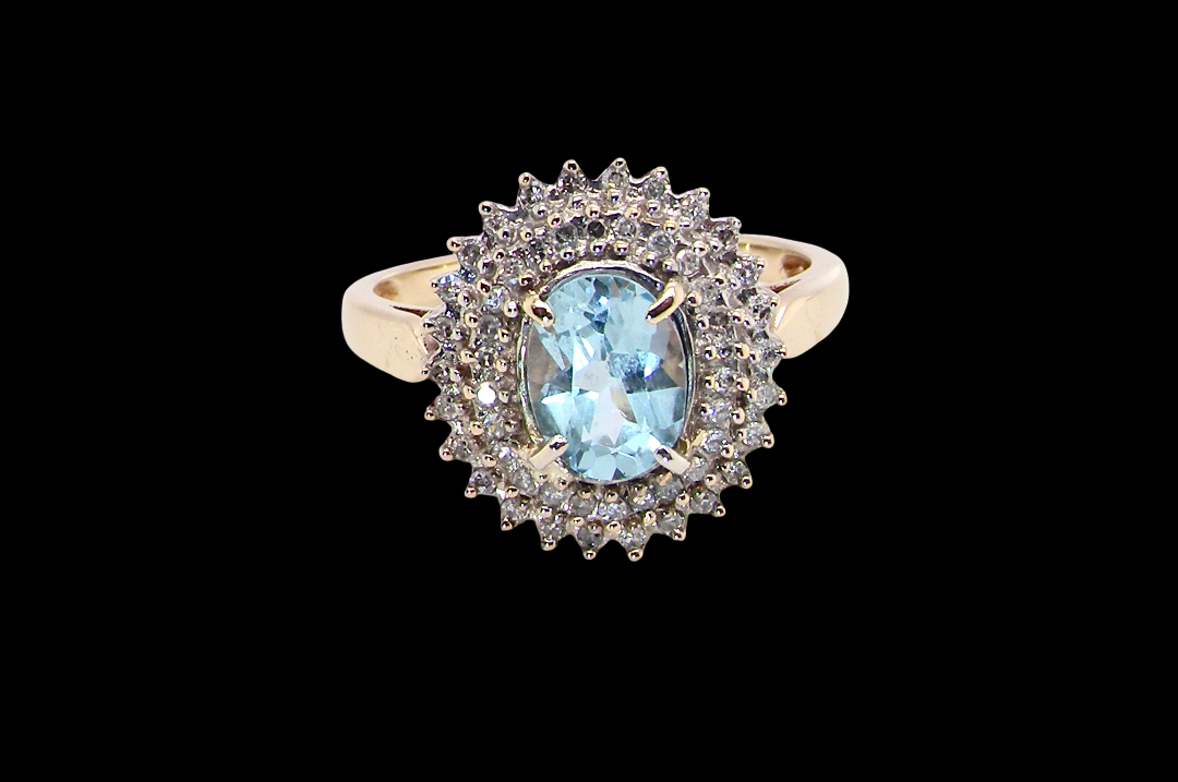 An impressive cluster ring that features to the centre an oval cut blue topaz gemstone, 8x6mm sky blue colour.
Complimented by a double halo of diamonds