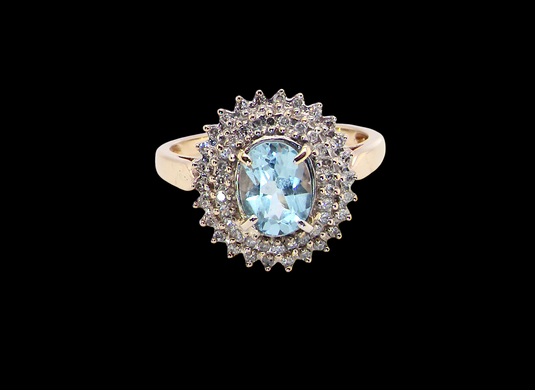 An impressive cluster ring that features to the centre an oval cut blue topaz gemstone, 8x6mm sky blue colour.
Complimented by a double halo of diamonds