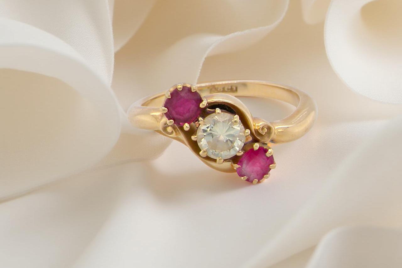 Gold ring with a central diamond and two rubies on a white fabric background