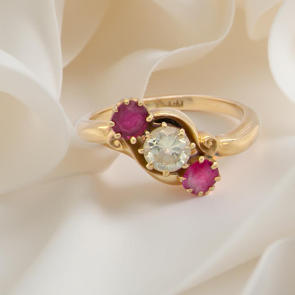 Gold ring with a central diamond and two rubies on a white fabric background