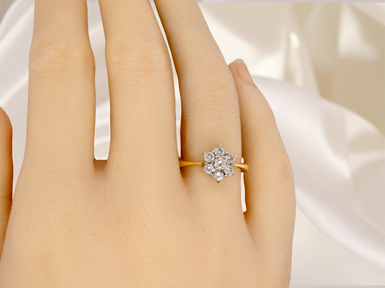 Gold ring with a diamond on a hand against a white satin background