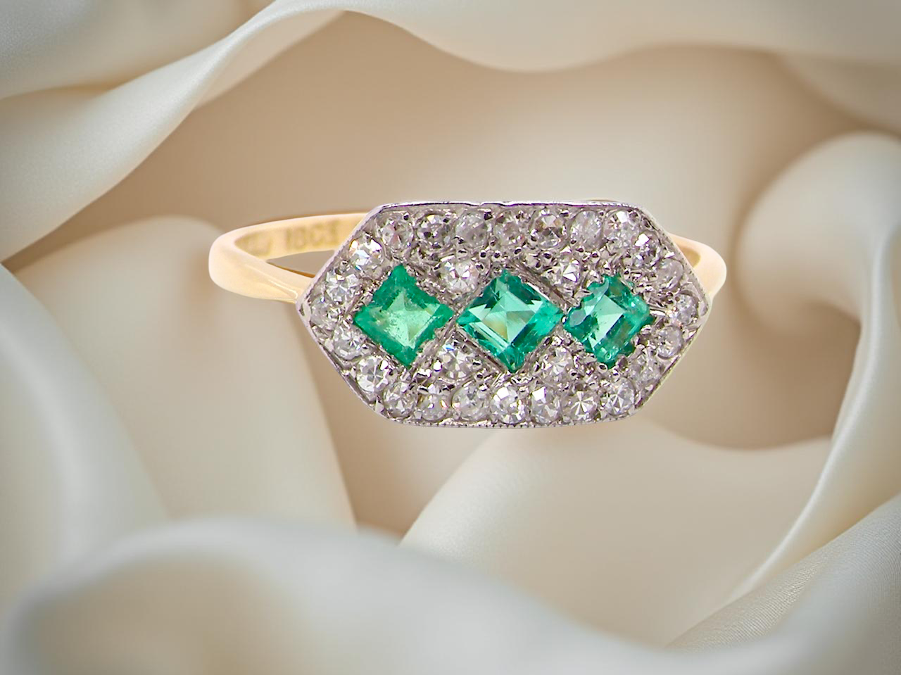 Edwardian era cluster ring, beautifully handcrafted with a trio of vibrant emeralds surrounded by a halo of antique old-cut diamonds.