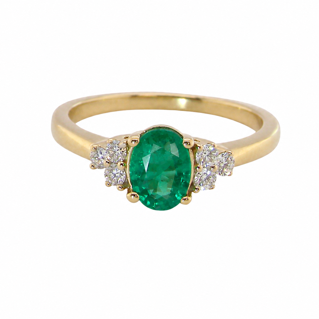 A yellow gold ring featuring an oval-cut green emerald center stone, flanked by small clusters of clear pavé diamonds, set against a plain white background.