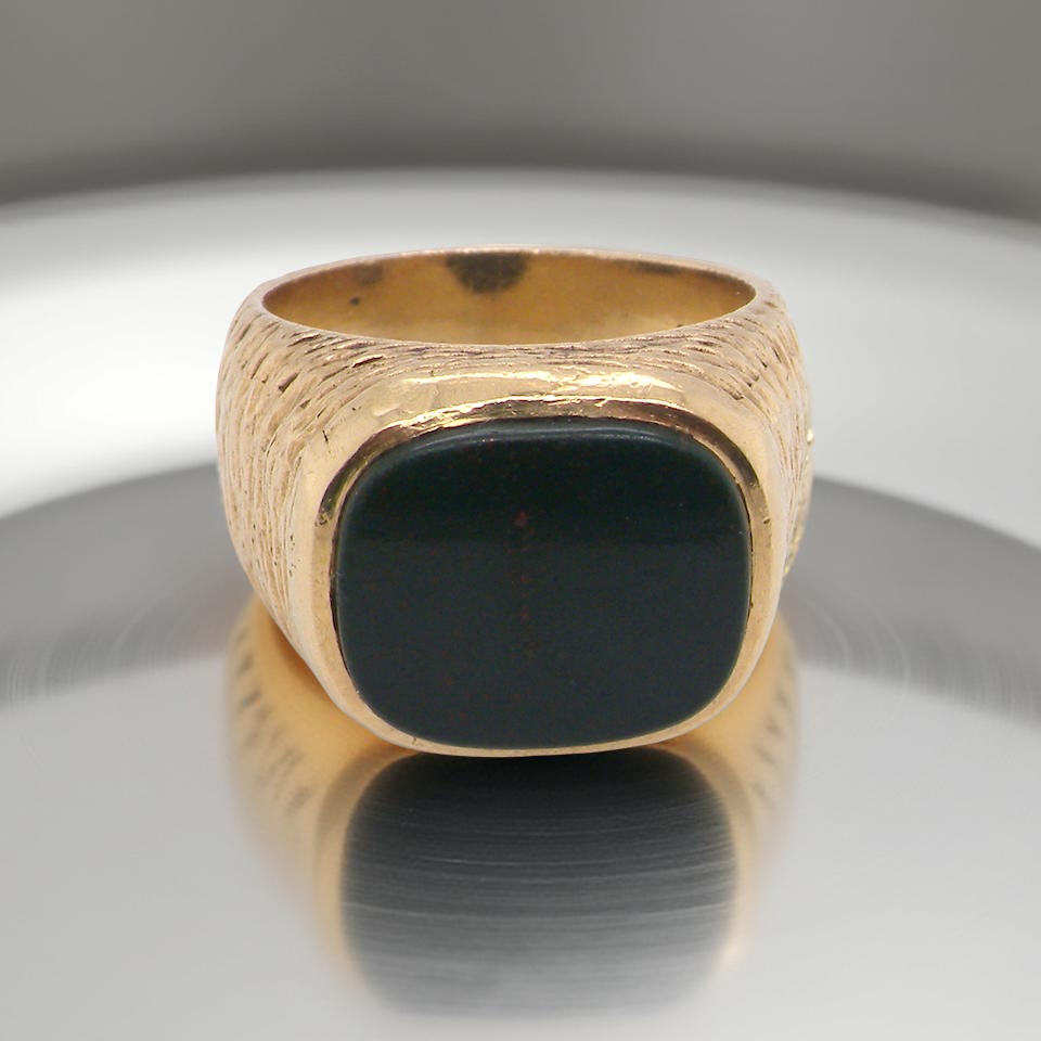 Gold ring with a black stone on a reflective surface