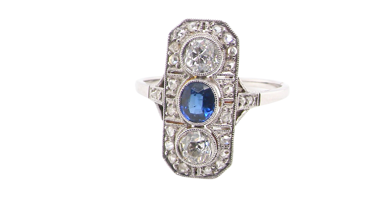 The plaque design has at its centre a mid to dark blue sapphire, 5x4mm (est 0.40 carats) mille grain set. Above and below to Old European Cut white diamonds. Each one estimated at 0.40 carats (4.8mm)