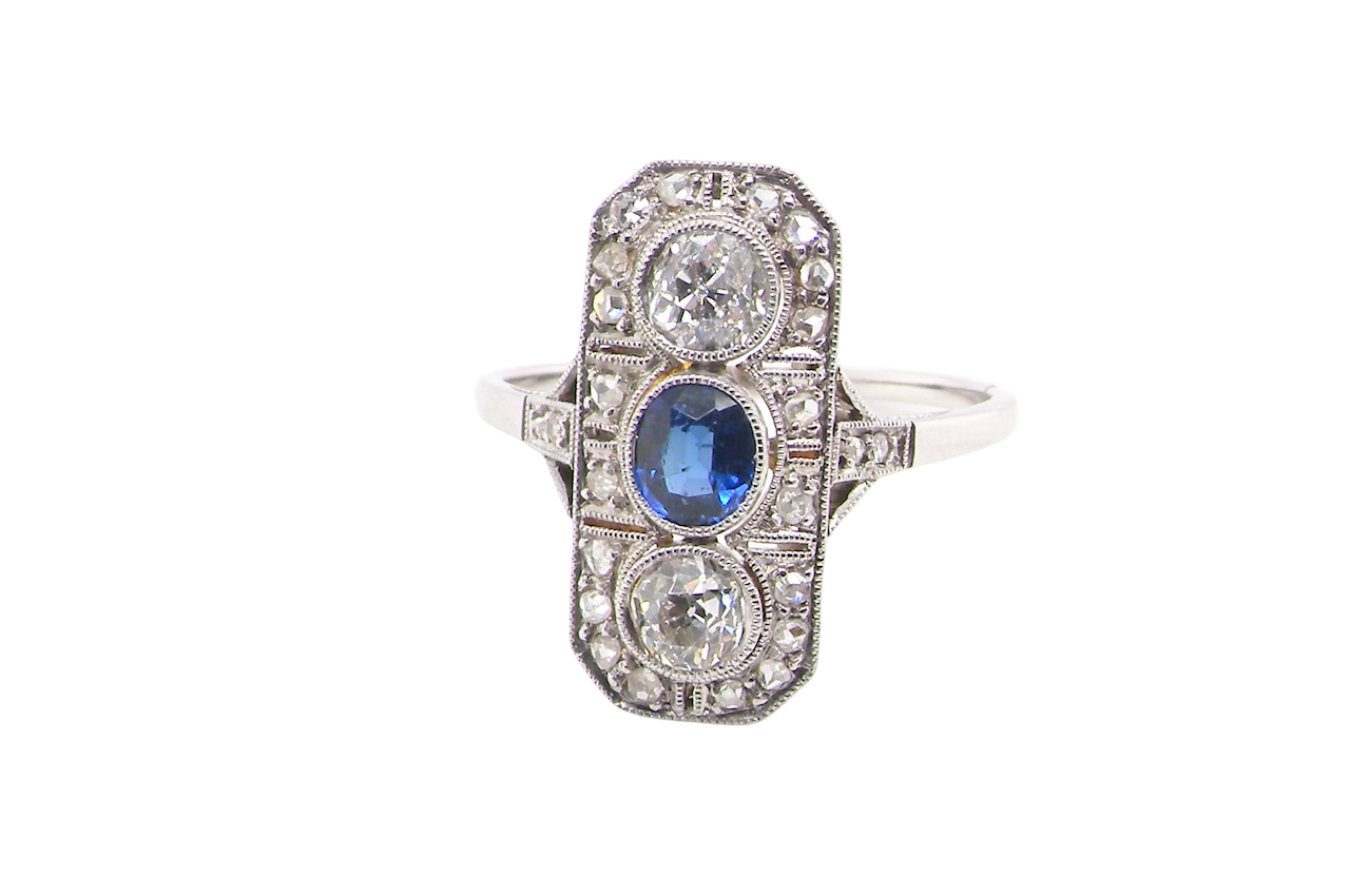 The plaque design has at its centre a mid to dark blue sapphire, 5x4mm (est 0.40 carats) mille grain set. Above and below to Old European Cut white diamonds. Each one estimated at 0.40 carats (4.8mm)