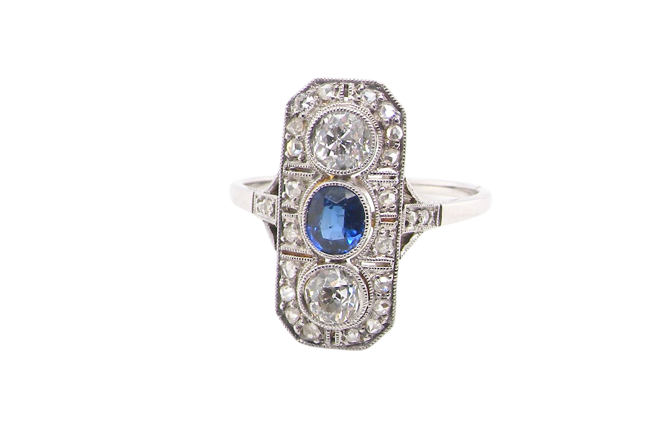 The plaque design has at its centre a mid to dark blue sapphire, 5x4mm (est 0.40 carats) mille grain set. Above and below to Old European Cut white diamonds. Each one estimated at 0.40 carats (4.8mm)