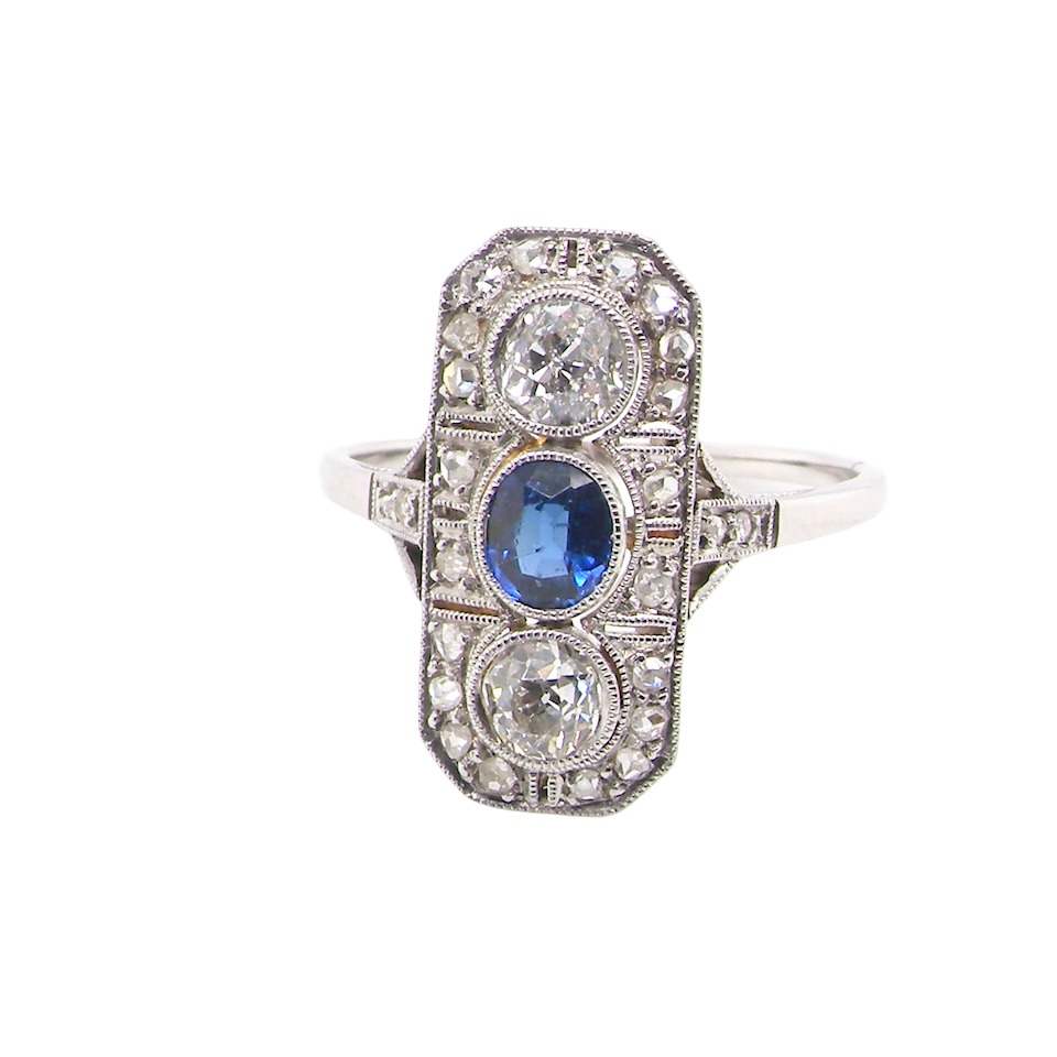 The plaque design has at its centre a mid to dark blue sapphire, 5x4mm (est 0.40 carats) mille grain set. Above and below to Old European Cut white diamonds. Each one estimated at 0.40 carats (4.8mm)