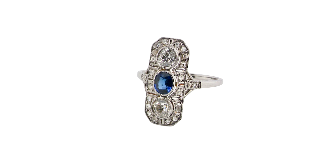 The plaque design has at its centre a mid to dark blue sapphire, 5x4mm (est 0.40 carats) mille grain set. Above and below to Old European Cut white diamonds. Each one estimated at 0.40 carats (4.8mm) Colour H-j, clarity Si.