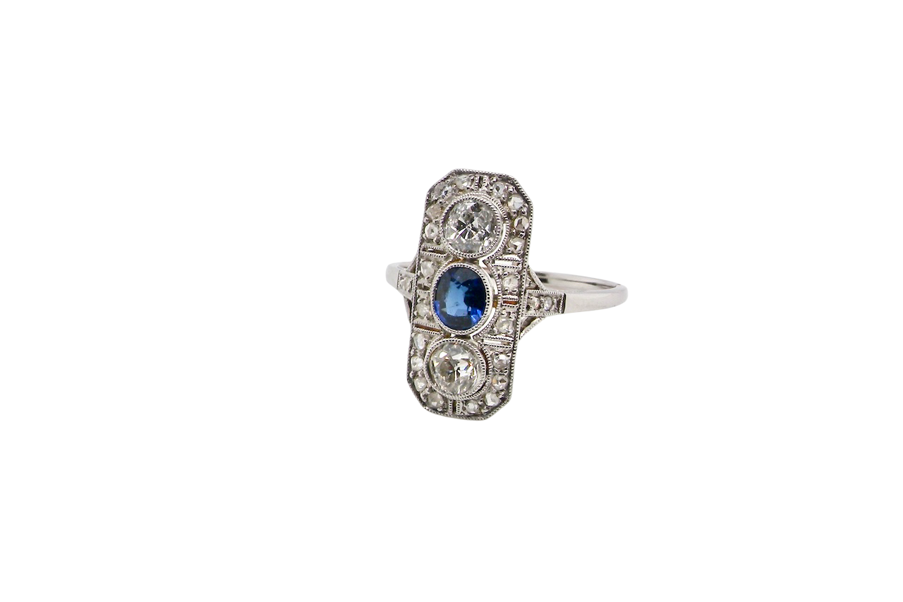 The plaque design has at its centre a mid to dark blue sapphire, 5x4mm (est 0.40 carats) mille grain set. Above and below to Old European Cut white diamonds. Each one estimated at 0.40 carats (4.8mm) Colour H-j, clarity Si.