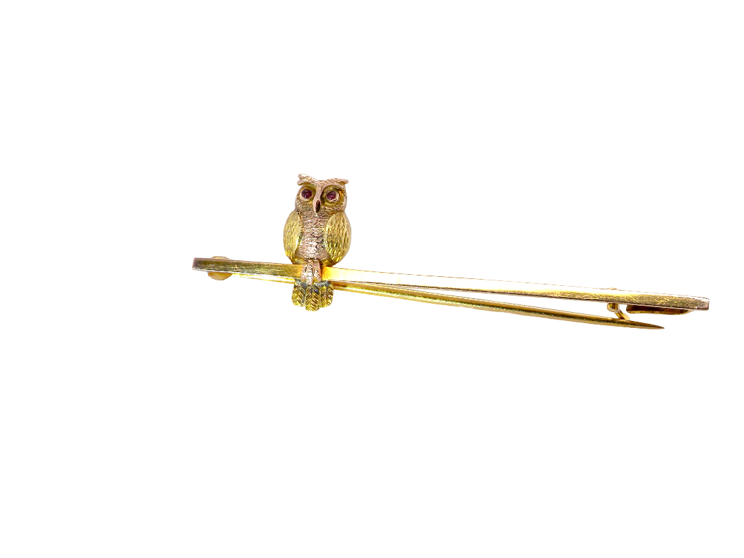 A gold owl pin perched on a thin gold bar, photographed against a solid white background.