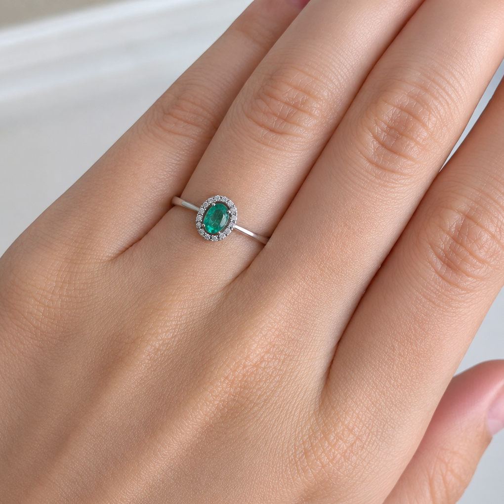 White gold ring with a green gemstone on a person's finger against a neutral background