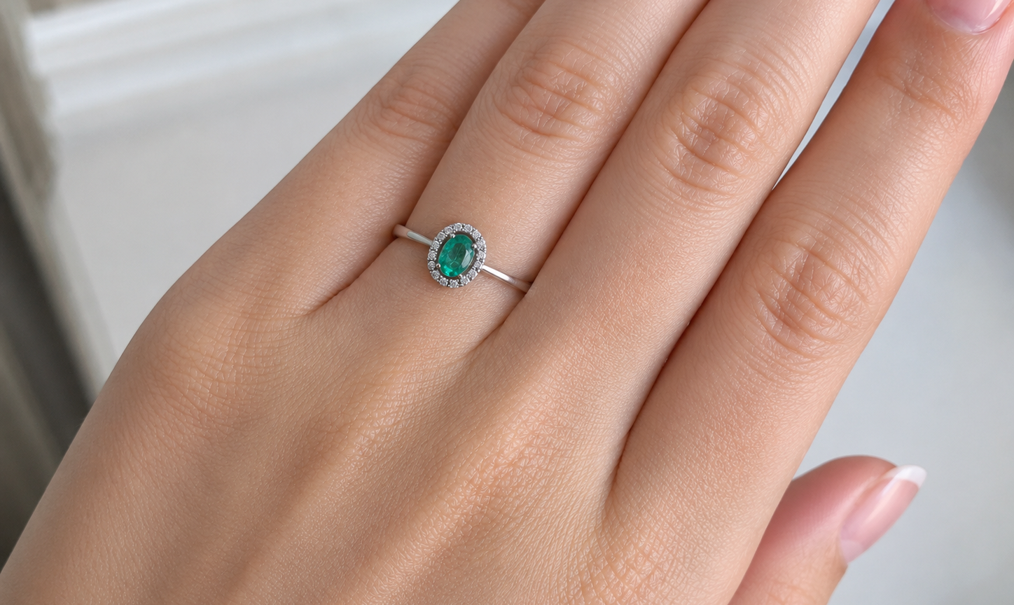 White gold ring with a green gemstone on a person's finger against a neutral background