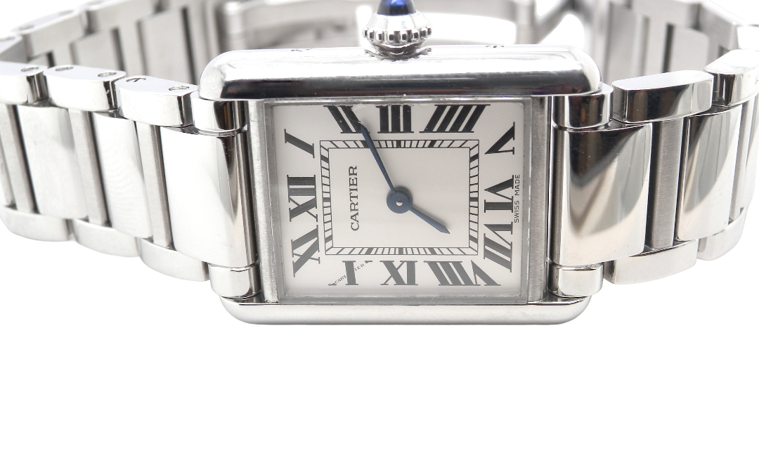 close view A womans stainless steel Cartier Tank Must wrist watch. Model number WSTA0051.
Silver coloured dial with Roman Numerals. Blue steeled hands. Case measures 29.5x22mm, case thickness 6.6mm. Quartz movement, synthetic sapphire button.