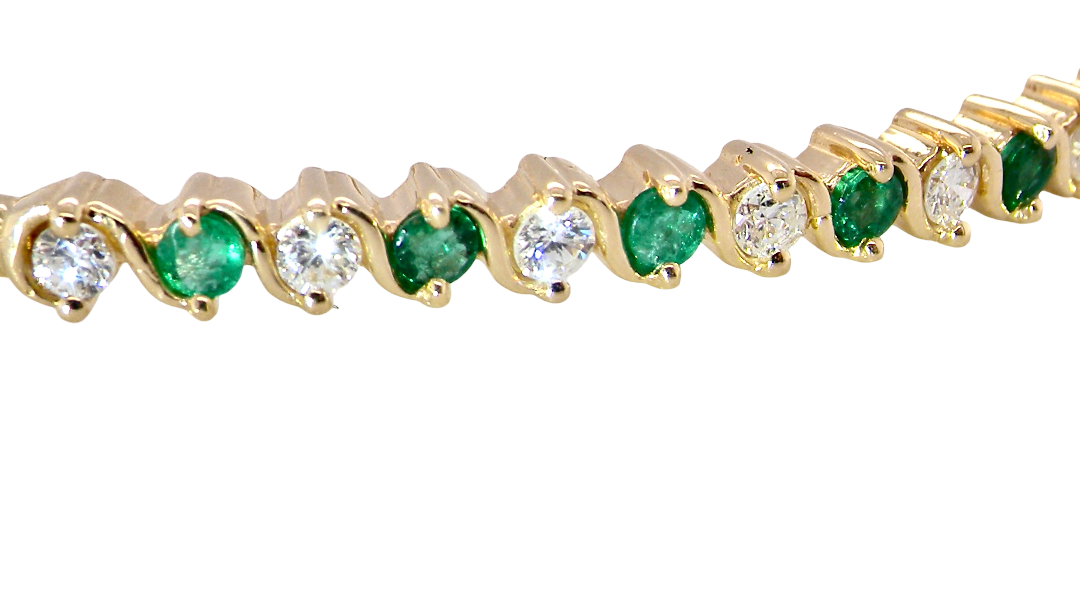 close view A yellow gold bangle. Features alternate emeralds and diamonds. Six 2.7mm emeralds and seven brilliant cut white diamonds, each 2.7mm (total diamond total 0.50 carats)
