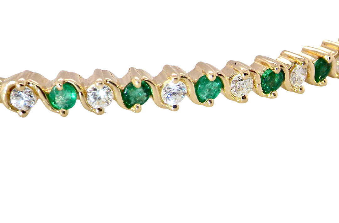 close view A yellow gold bangle. Features alternate emeralds and diamonds. Six 2.7mm emeralds and seven brilliant cut white diamonds, each 2.7mm (total diamond total 0.50 carats)