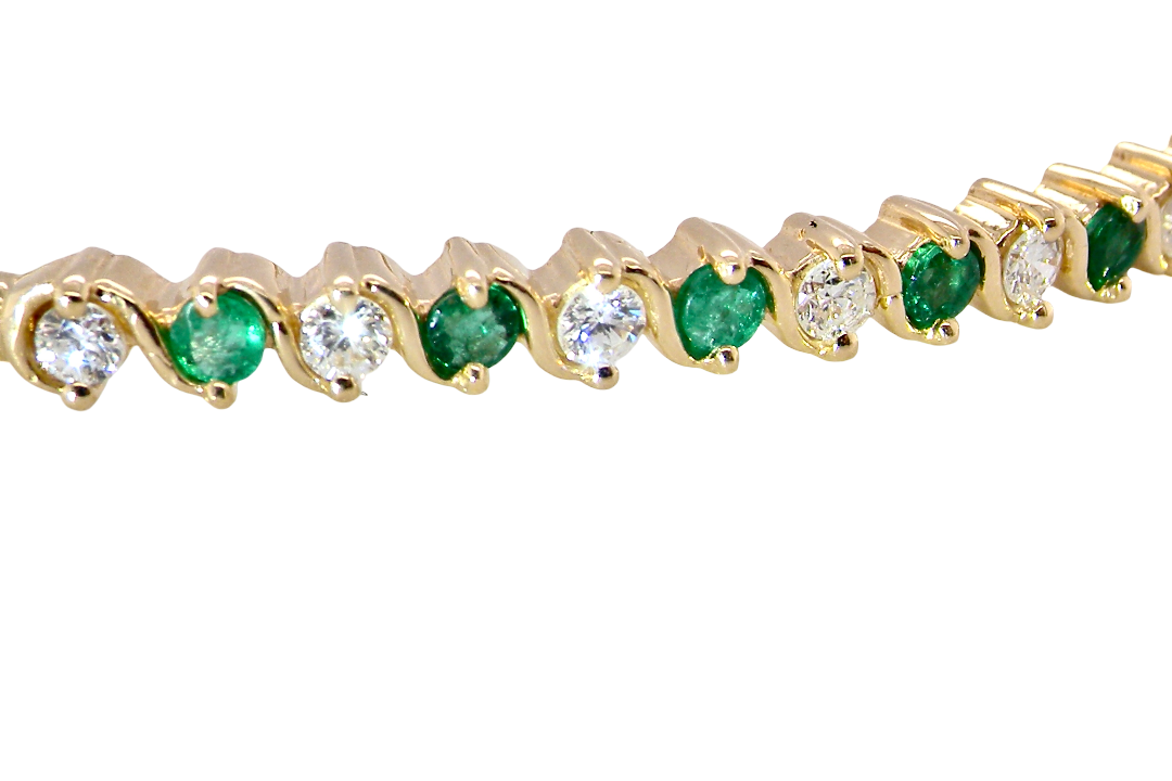 close view A yellow gold bangle. Features alternate emeralds and diamonds. Six 2.7mm emeralds and seven brilliant cut white diamonds, each 2.7mm (total diamond total 0.50 carats)