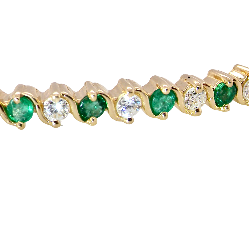 close view A yellow gold bangle. Features alternate emeralds and diamonds. Six 2.7mm emeralds and seven brilliant cut white diamonds, each 2.7mm (total diamond total 0.50 carats)
