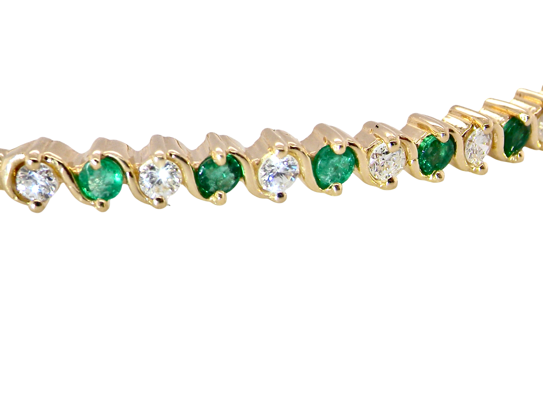 close view A yellow gold bangle. Features alternate emeralds and diamonds. Six 2.7mm emeralds and seven brilliant cut white diamonds, each 2.7mm (total diamond total 0.50 carats)