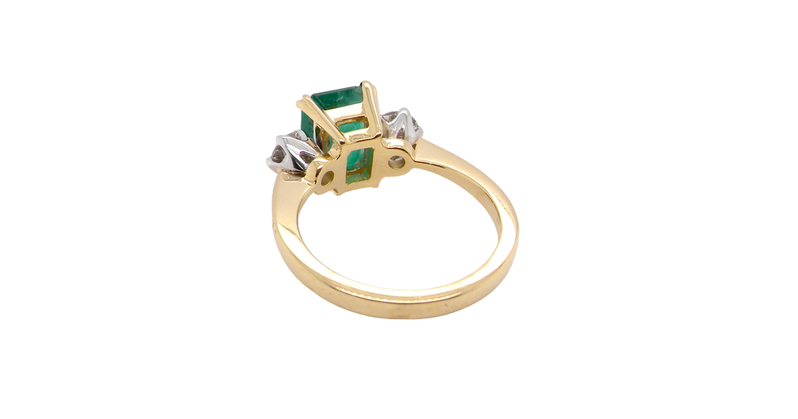 An exceptional three-stone ring featuring a vibrant step-cut emerald to the centre, measuring 8.6 x 7.0mm and weighing approximately 2.10 carats. The emerald displays a beautiful grass-green colour and is secured in a classic four-claw setting.