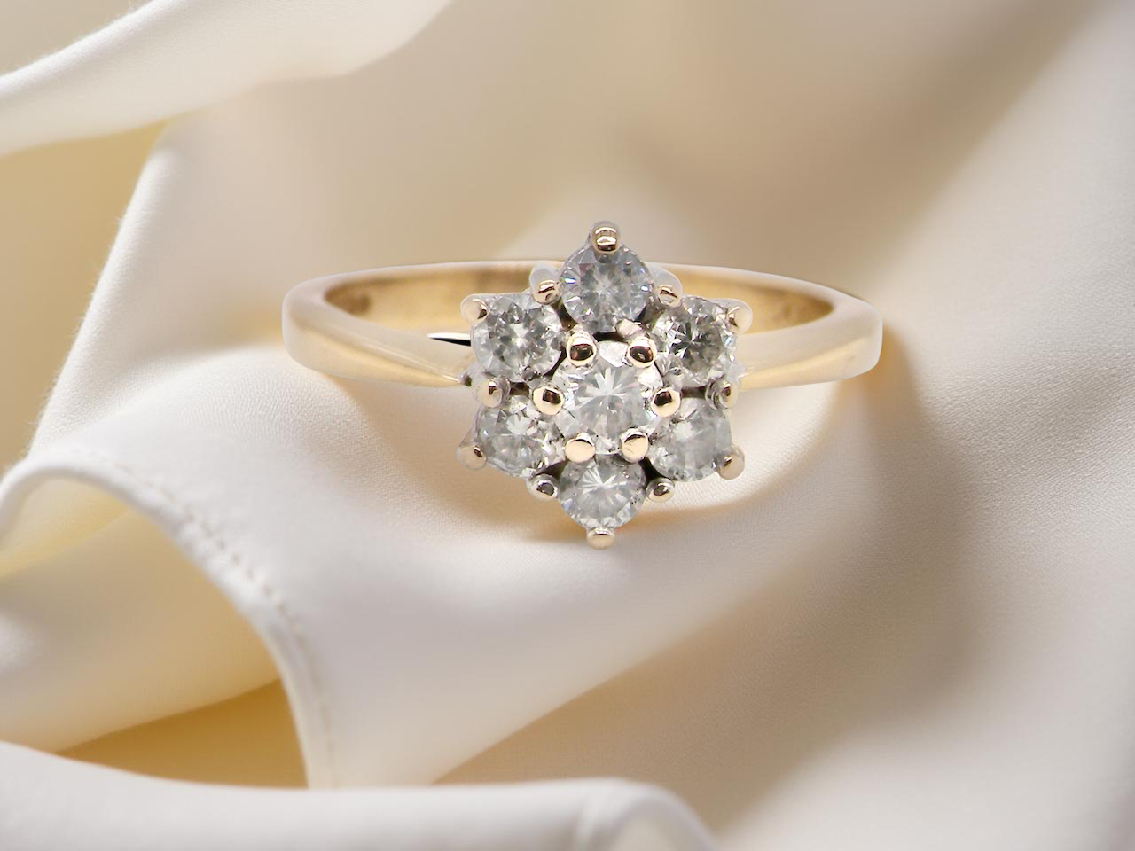 Gold ring with diamond cluster on a soft white fabric background