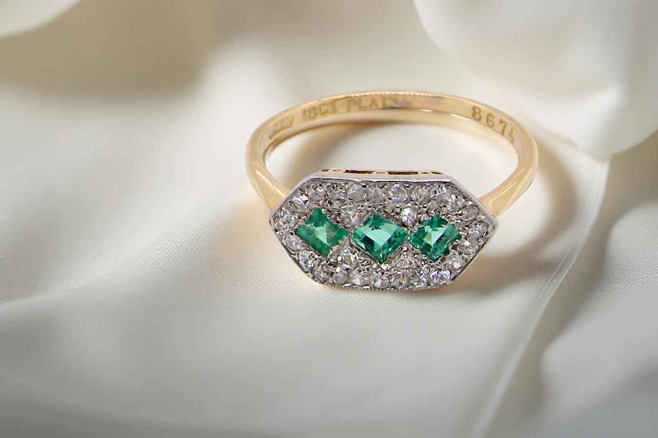 fine Edwardian era cluster ring, beautifully handcrafted with a trio of vibrant emeralds surrounded by a halo of antique diamonds.