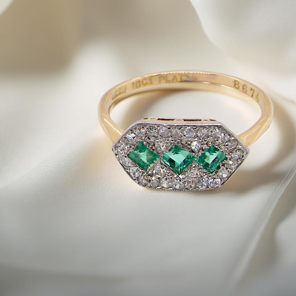 fine Edwardian era cluster ring, beautifully handcrafted with a trio of vibrant emeralds surrounded by a halo of antique diamonds.
