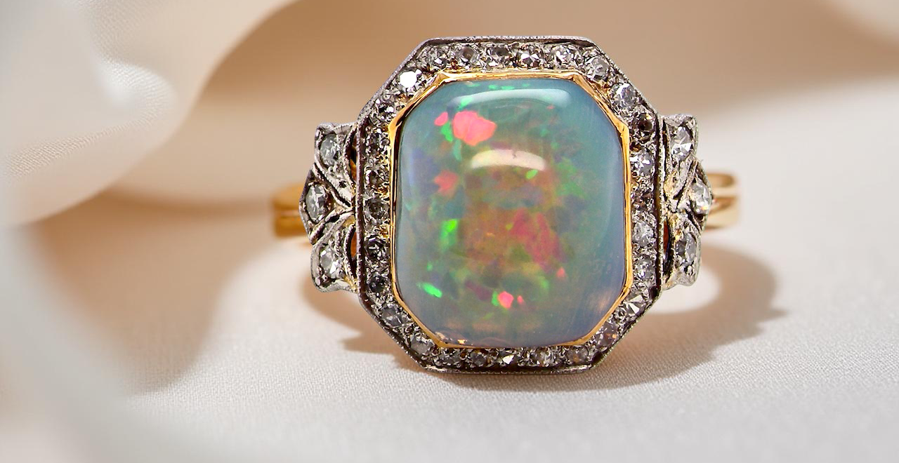 fine cabouchon cut opal shown is cushion shaped, measures 15x13 (5.78 carats) displaying a mass of vibrant colours, from flashes of fireglow orange, luminous greens, and lavender purples.