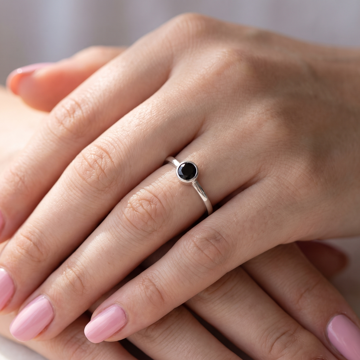 hand A 9 carat white gold solitaire ring. Features a round dark blue sapphire, 4.6mm diameter (est 0.38 carats) Rim set.