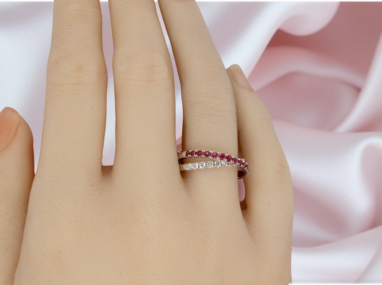 Close-up of a hand wearing two rings with a soft pink fabric background