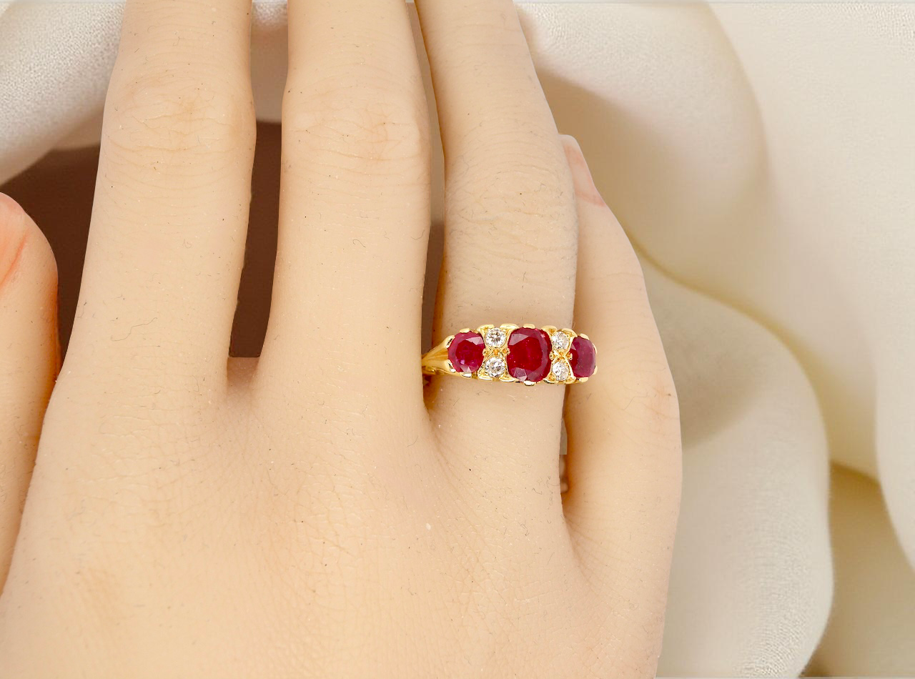 Gold ring with red gemstones on a person's finger against a soft white background