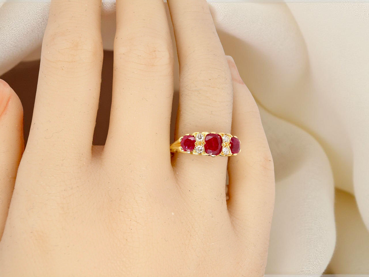 Gold ring with red gemstones on a person's finger against a soft white background
