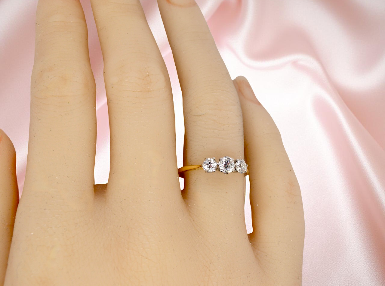 Silver ring with three diamonds on a finger against a pink satin background