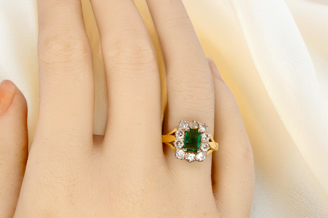 hand A cluster ring that features a rectangular emerald centre stone, 7x5mm . Deep green colour, natural inclusions that can be seen under an eye glass, but not easily visible via the naked eye.