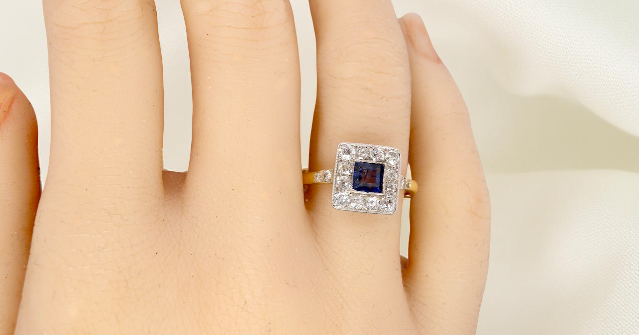hand A fine Art Deco cluster ring. The centre stone a square sapphire 5x5mm (est 0.50 carats) in a mille grain setting.