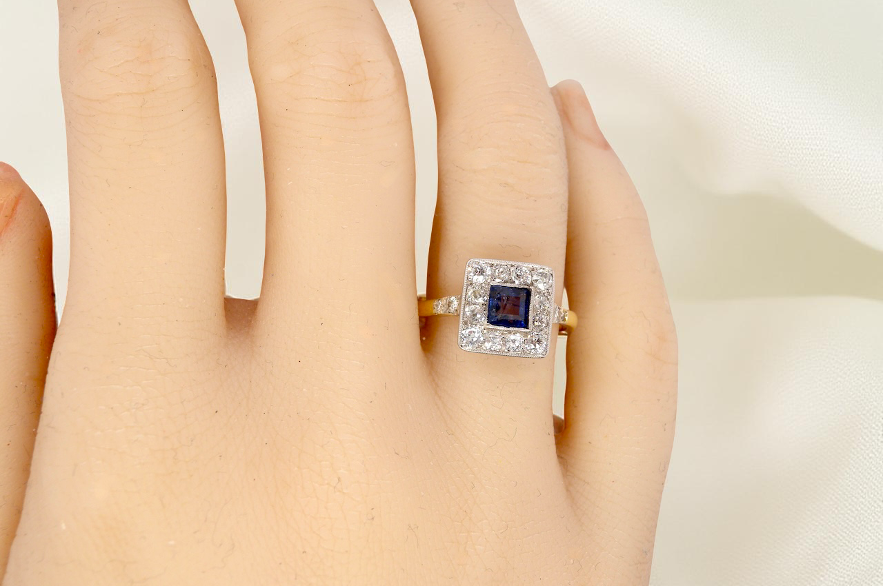 hand A fine Art Deco cluster ring. The centre stone a square sapphire 5x5mm (est 0.50 carats) in a mille grain setting.