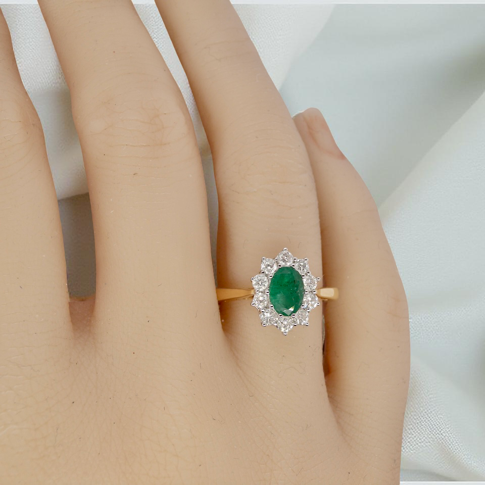 hand A fine traditional emerald and diamond cluster ring, featuring a vibrant oval-cut emerald to the centre measuring approximately 7 × 5 mm