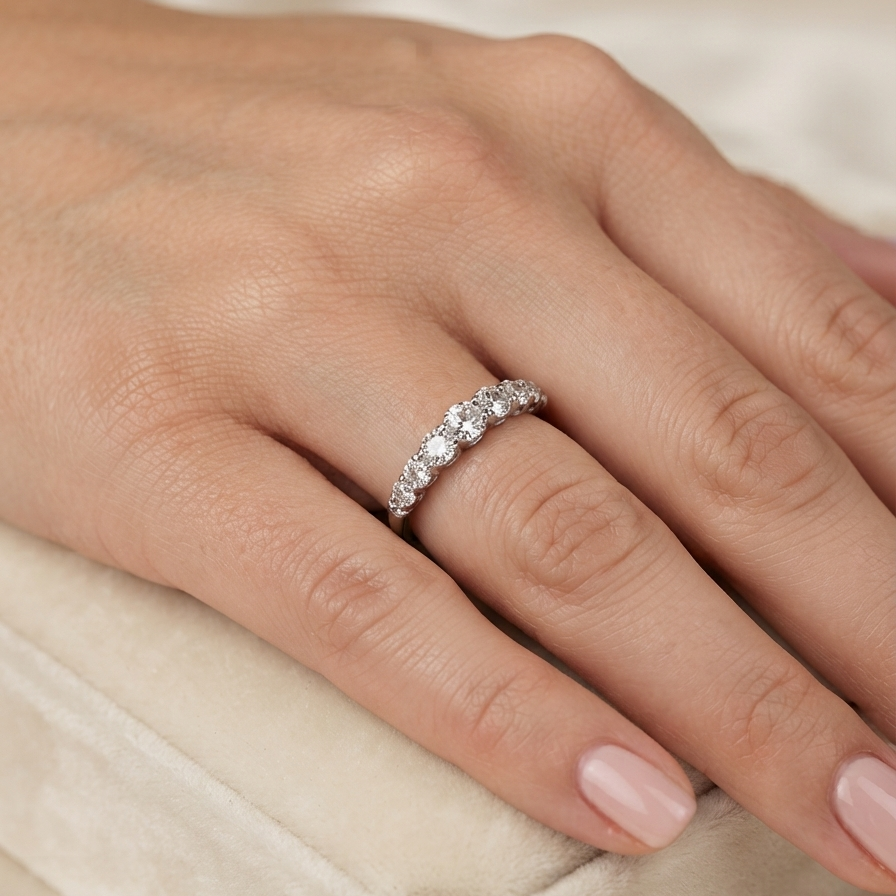 A close-up of a hand wearing a eternity ring set with clear round-cut gemstones, resting on a soft cream velvet jewelry box.