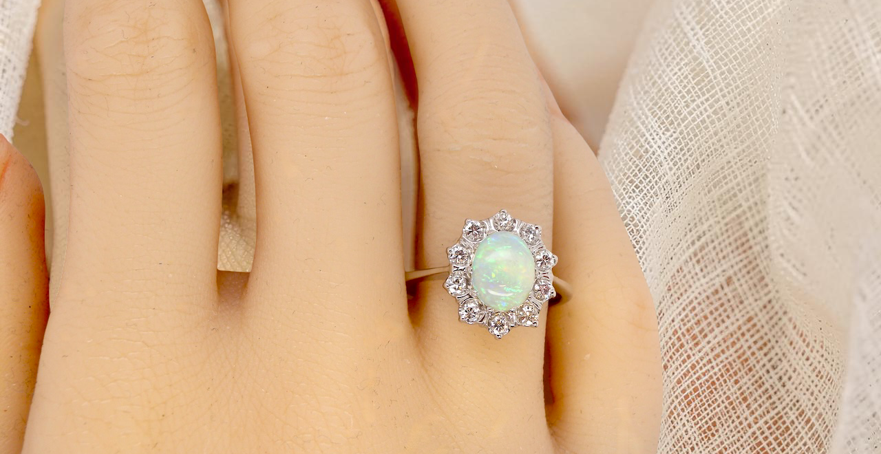 hand A lovely white gold cluster ring. Features to the centre an oval white opal, 9x7mm, with an excellent play of colour.