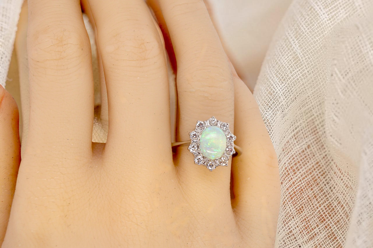 hand A lovely white gold cluster ring. Features to the centre an oval white opal, 9x7mm, with an excellent play of colour.