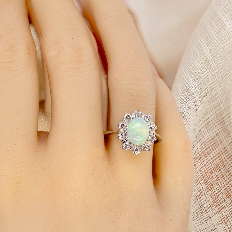 hand A lovely white gold cluster ring. Features to the centre an oval white opal, 9x7mm, with an excellent play of colour.