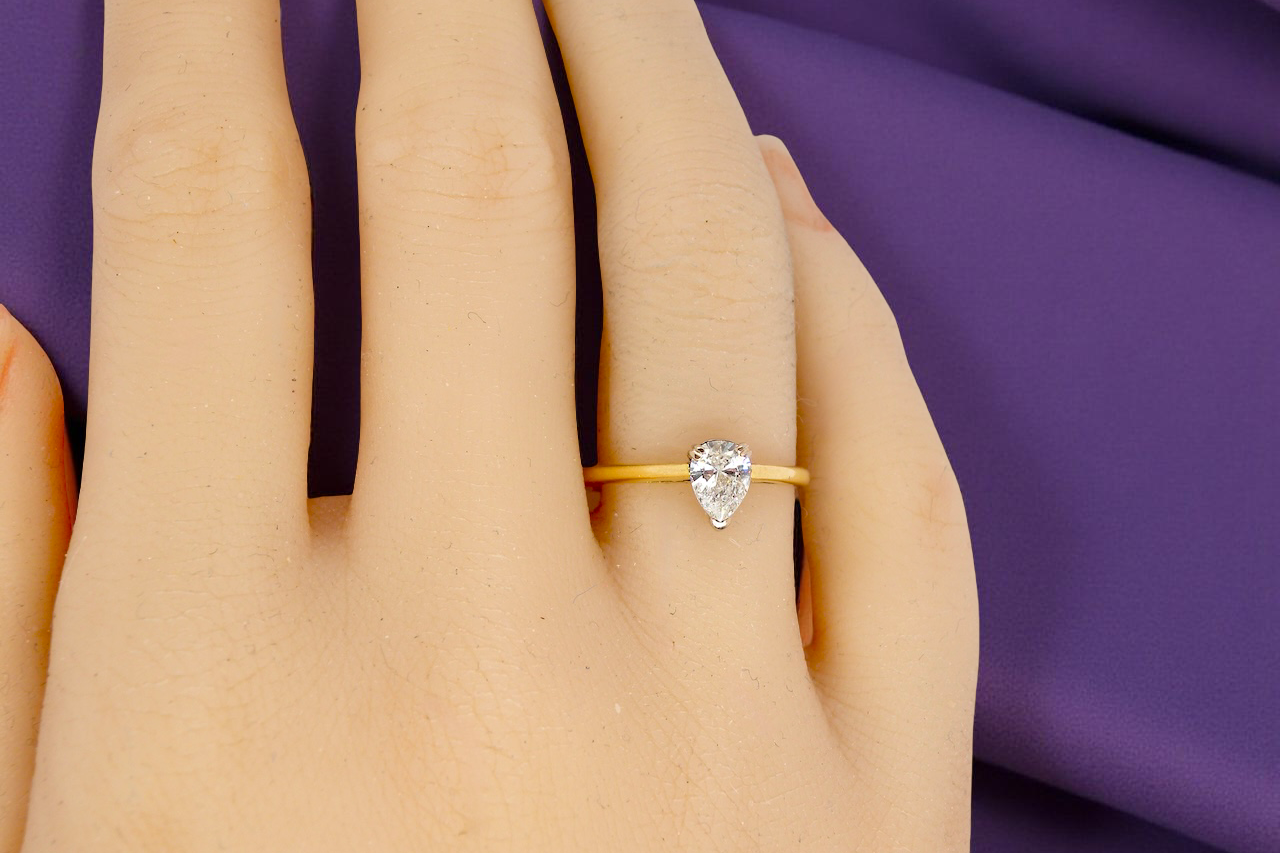 Gold ring with a pear-shaped diamond on a hand against a purple fabric background
