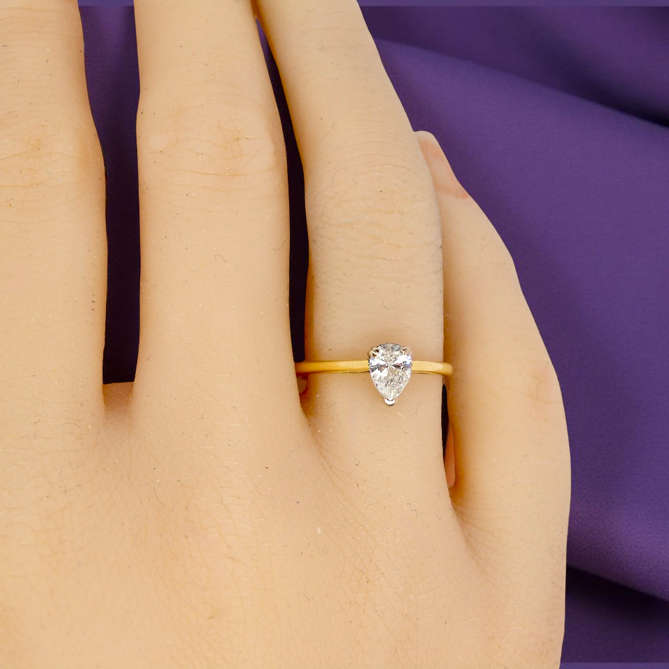 Gold ring with a pear-shaped diamond on a hand against a purple fabric background