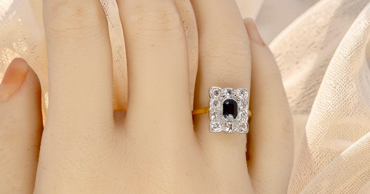 hand A rectangular cluster ring that features in its centre a cushion shaped dark blue sapphire, that measures 5x3.5mm (est 0.30 carats)