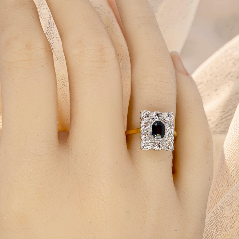 hand A rectangular cluster ring that features in its centre a cushion shaped dark blue sapphire, that measures 5x3.5mm (est 0.30 carats)
